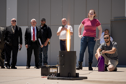 Professors, students and Thomas A. Lockhart gather outside observing a flame from a heat tolerance test