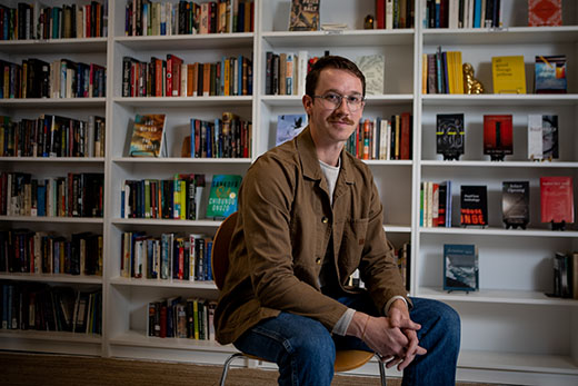 A photo of Patrick Ramsay sitting in front of books at his bookstore the Happy Magpie Book & Quill.