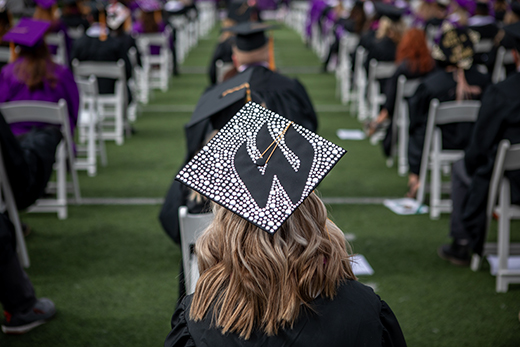 A graduate photographed from behind with a bejeweled graduation cap at an outdoor ceremony