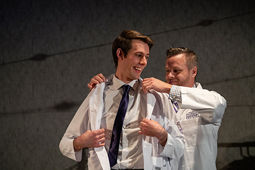 A Weber State student smiles as he receives his white coat from a professor at the first Physician Assistant White Coat Ceremony.