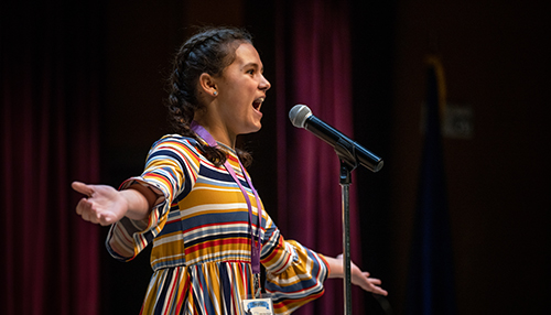 A young female student is sharing a story on stage at Weber State's Storytelling Festival. 
