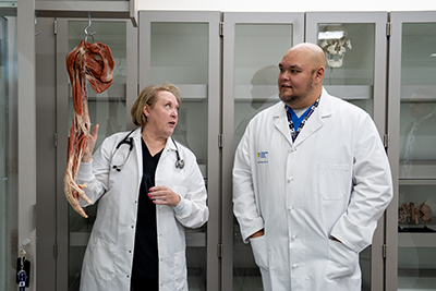 Two WSU faculty in white lab coats analyze the anatomy of a human arm