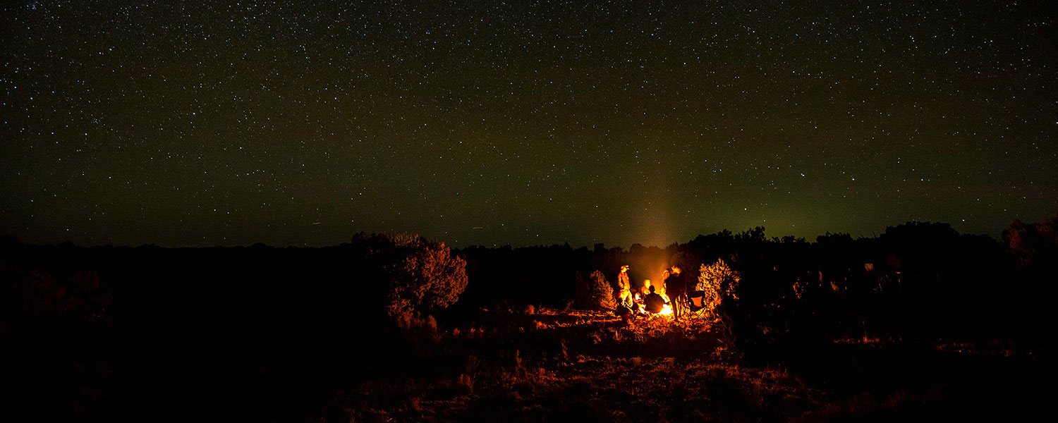 students on camping trip in front of fire under stars