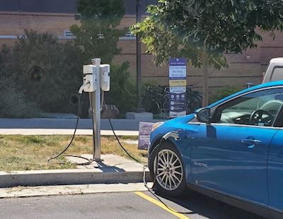Blue car in front of an EV charging station outside of a Weber State brick building. 